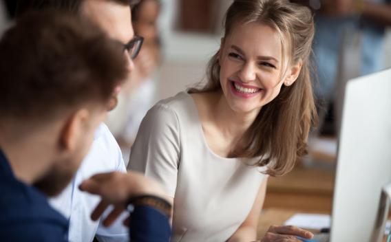 Smiling happy young woman talking with male colleagues at shared workplace