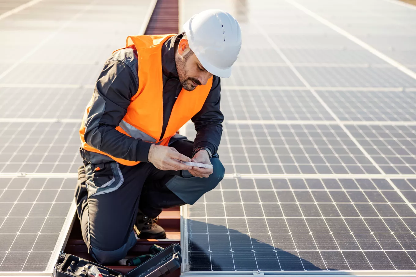 A worker on the rooftop picking screws from toolbox to install solar panels.