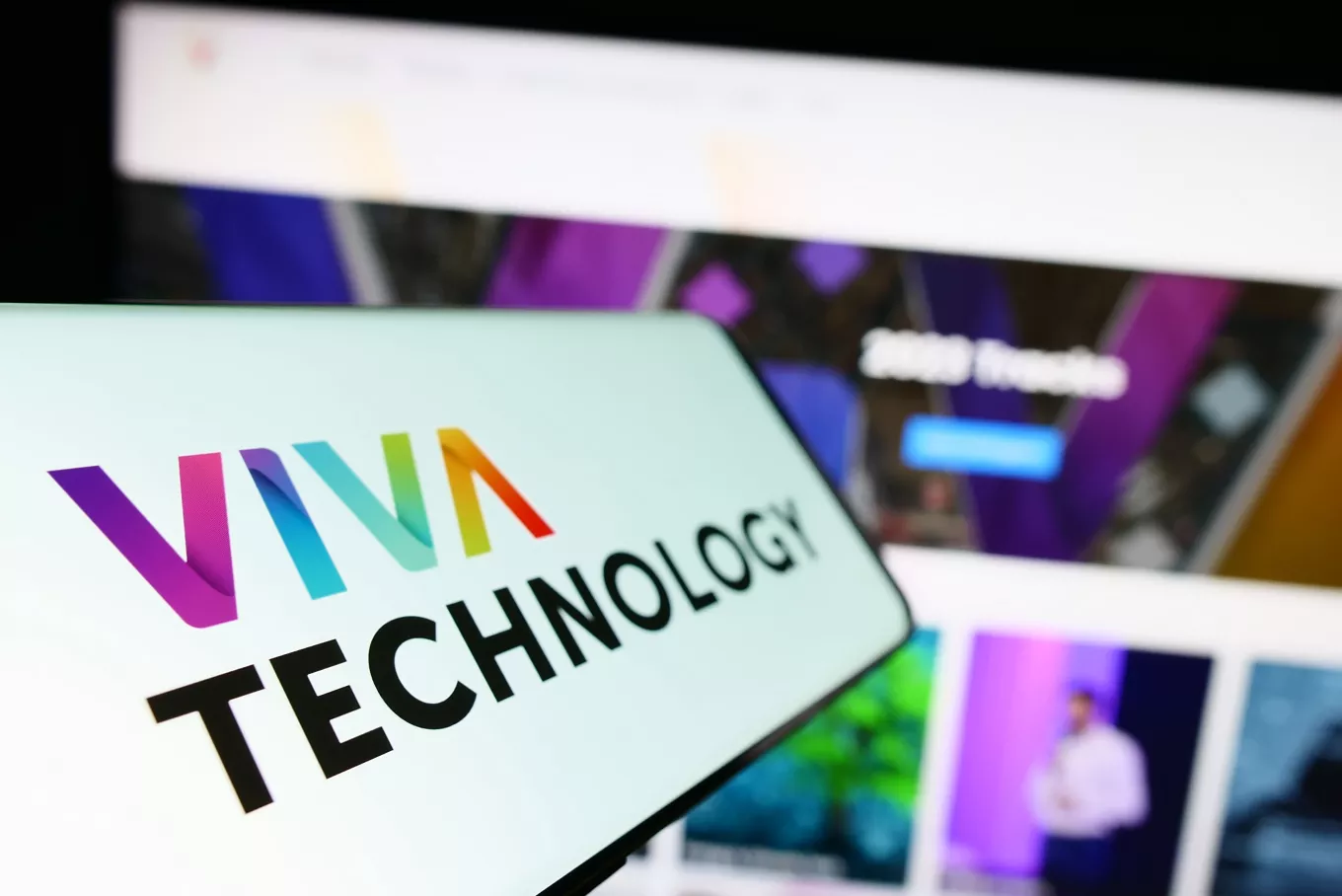 Smartphone with logo of French conference Viva Technology (VivaTech) on screen in front of business website. Focus on left of phone display