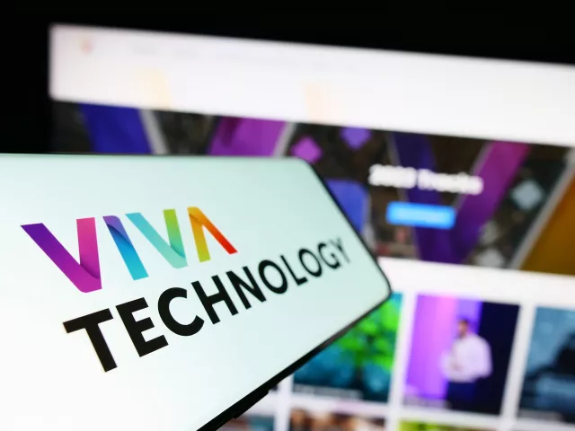 Smartphone with logo of French conference Viva Technology (VivaTech) on screen in front of business website. Focus on left of phone display
