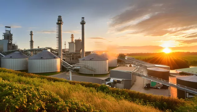 A bustling biomass energy facility at sunset, featuring large metal silos used for storing and processing organic matter into renewable energy.