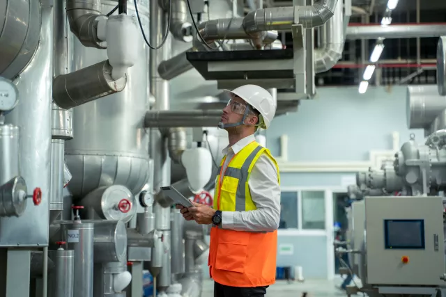 Professional worker of modern factory using laptop controlling program to automatic machinery. Engineering with laptop Programmable Logic Controller to manage large machine working full automatic.